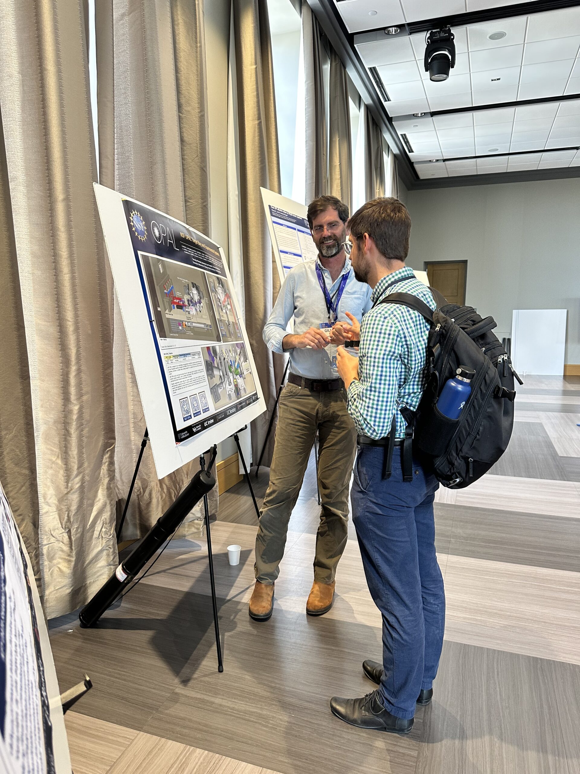 Two conference attendees discuss a research poster during a poster session in a bright conference venue.