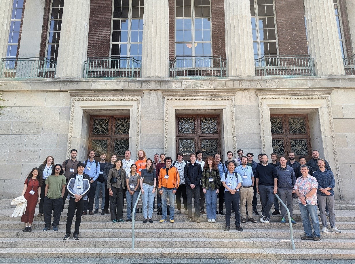 Group photo of conference attendees gathered on the steps of Rush Rhees Library at the University of Rochester. Participants face the camera in front of the library's grand columns and historic entrance on a sunny day.