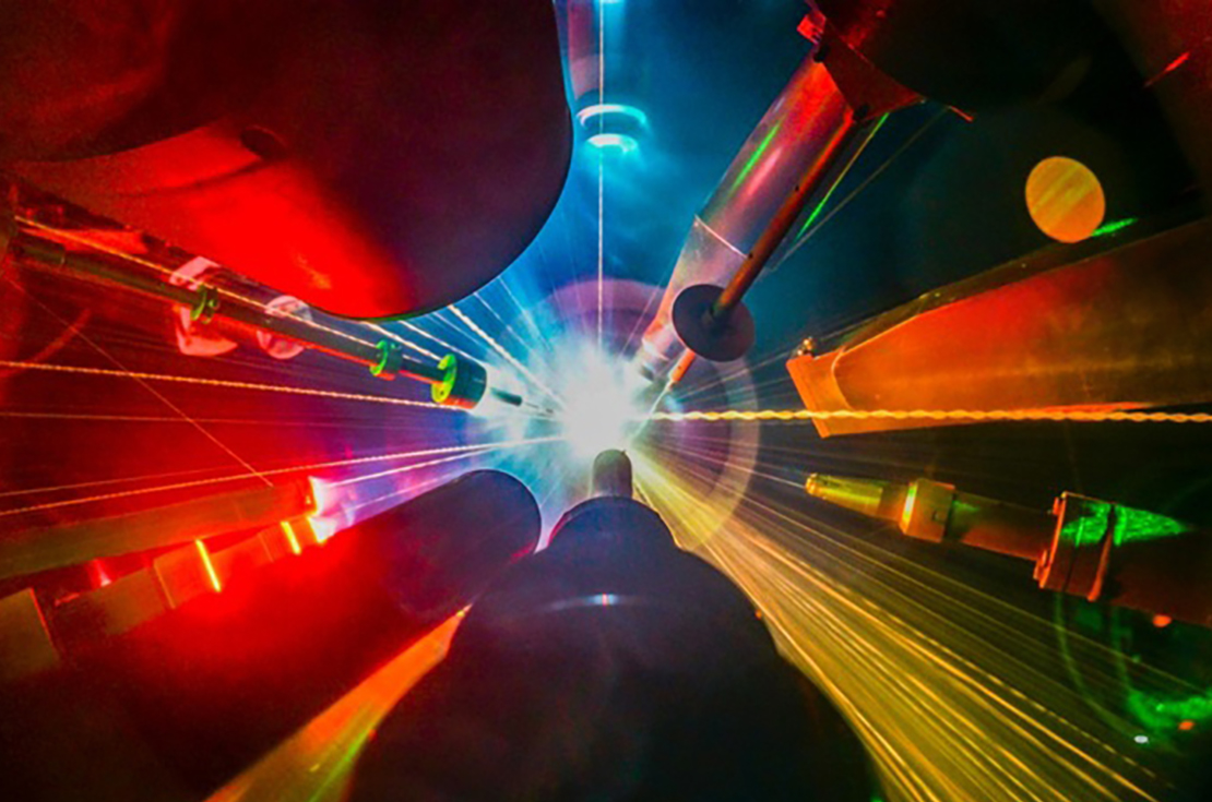 Photograph of a target shot inside OMEGA target chamber, with streaks shooting outward from the central a bright central light illuminating instruments in colorful reds, oranges, blues and greens.